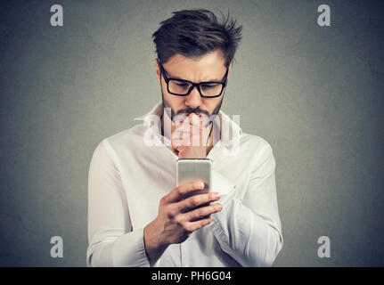 Clueless junger Mann Probleme mit seinem Smartphone suchen beschäftigt Stockfoto