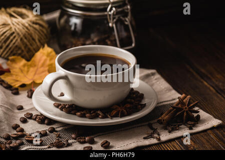 Weiße Tasse Kaffee mit verschiedenen Gewürzen, Bohnen und gelben Blätter im Herbst auf dunklem Hintergrund Stockfoto