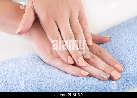 Junge Frau Finger mit orange Maniküre auf die Nägel Hand auf Blau Handtuch in Beauty Studio. Close Up, selektiver Fokus Stockfoto