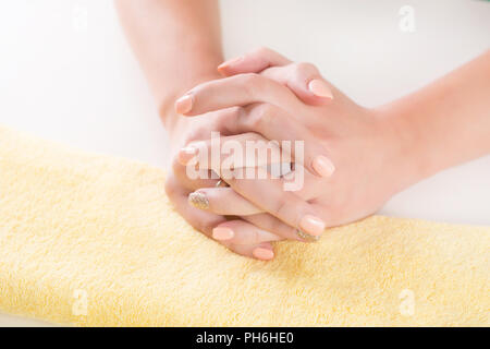 Junge weibliche Hand mit orange Maniküre auf Nägeln gekreuzten Fingern auf gelb Handtuch in Beauty Studio. Mode und Maniküre Konzept. Nahaufnahme Stockfoto