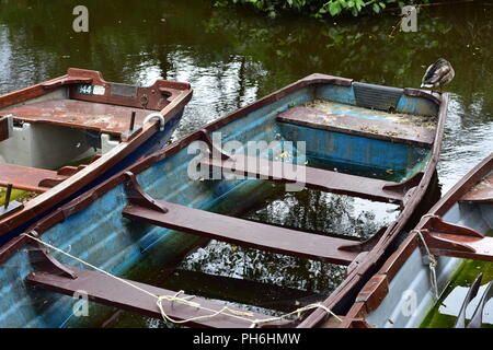 Verwitterte offene Boote mit Bänken teilweise mit Regen Wasser schwimmend auf ruhigen Fluss gefüllt. Stockfoto
