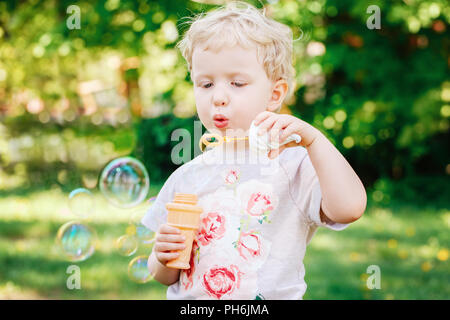 Portrait von niedlichen Lustige kleine blonde Kaukasier Kind girl Toddler, stehen im grünen Wald Feld Wiese bläst Seifenblasen, hellen Sommertag, su Stockfoto