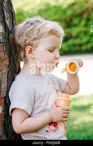 Portrait von niedlichen Lustige kleine blonde Kaukasier Kind girl Toddler, stehen im grünen Wald Feld Wiese bläst Seifenblasen, hellen Sommertag, su Stockfoto