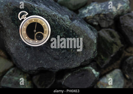 Nahaufnahme von einem schönen Retro Style schwarz und silber Taschenuhr Festlegung auf nassen grüne Steine Stockfoto