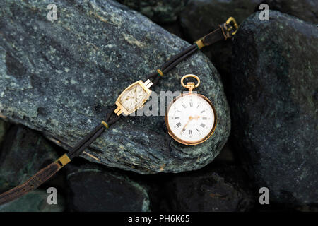 Einstellen der Uhren auf nassen grüne Steine mit einem Classic Gold Taschenuhr und eine Armbanduhr mit verschlissenen Riemen Stockfoto