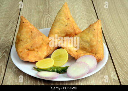 Punjabi Veg Samosa mit Zwiebel und Zitronenscheiben mit grünem Chili und Chutney auf hölzernen Hintergrund, Samosa ist ein beliebter Street Food in Indien Stockfoto