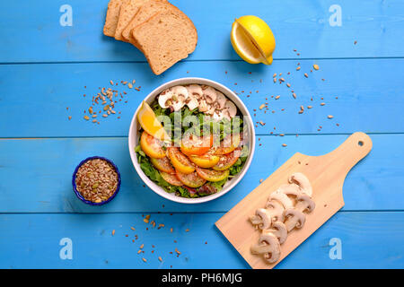 Ansicht von oben in eine Schüssel gemischter Salat mit Tomaten, Pilze, Salat und Samen mit Brot auf einem Holztisch Stockfoto