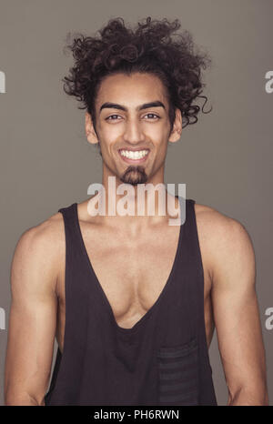 Fröhliche Curly-Haired athletischen Mann gegen Grau Stockfoto