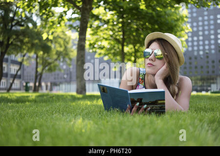 Nachdenkliches Mädchen liegt auf dem grünen Rasen mit Buch Stockfoto