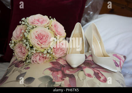 Bräute rosa Rose wedding bouquet neben ihrem Hochzeitstag Schuhe an Ihrem Hochzeitstag, zusammen sitzen auf einem Kissen. Stockfoto