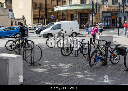 Fahrräder abgestellt und am Rand der Southgate Einkaufsviertel der Stadt Bath mit Passanten und Verkehr im Hintergrund gesichert Stockfoto