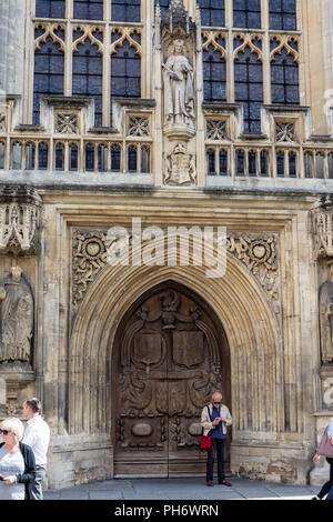 Mann stand in der geschnitzte Tür der Abtei von Bath mit seinem Mobiltelefon mit Passanten Stockfoto