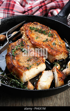 Gebratenes Schweinefleisch steak in Öl mit Kräutern und Knoblauch in einen Schnitt in die Pfanne. Stockfoto