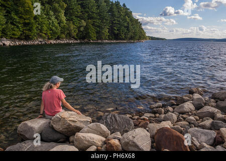 Frau sitzt am Ufer des Quabbin Reservoir in New Salem, Massachusetts Stockfoto