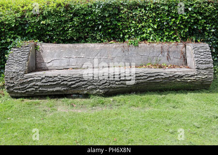 Eine ungewöhnliche Park Sitz aus einem Baumstamm mit einem Rasen auf der Vorderseite und eine Hecke im Hintergrund. Stockfoto