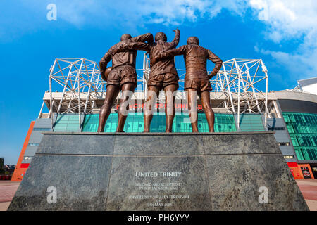 MANCHESTER, Großbritannien - 19 Mai 2018: Die United Trinity Bronze Skulptur, die mit George Best und Denis Law und Sir Bobby Charlton vor alten Tr aus Stockfoto