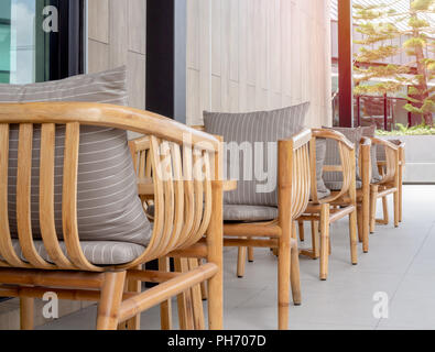 Zeile der hölzernen Sessel, Kissen, Holz- runde Tische auf Glas Fenster und modernen Holzmöbeln Wand auf im Hintergrund. Stockfoto