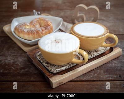 Zwei Tassen heißen Kaffee und süßes Brot auf weiße Platte auf Holz Tablett mit Holz-/Herz auf hölzernen Tisch Hintergrund. Stockfoto