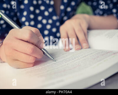 Close-up Hand mit einem Stift und Lesen Buch. Frau mit Polka Dot shirt lernen und merken Mit konzentrieren sich auf ein Buch. Stockfoto