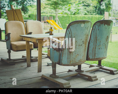 Vintage theater Sitze mit Holztisch auf Holzboden auf Green Park Hintergrund im Retro-stil Cafe. Einzigartige Mix und Match Möbel Stil Konzept. Stockfoto