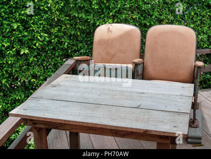 Vintage theater Sitze mit Holztisch auf hölzernen Terrasse auf Green Bush Hintergrund. Einzigartige Mix und Match Möbel Stil Konzept. Stockfoto