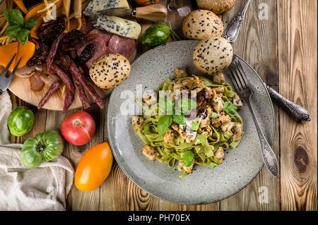 Pasta Pesto mit Fleisch und Pilzen, einer Auswahl an Käse, geräuchertem Fleisch und Wurst, Gemüse und würzige Kräuter auf einem Holztisch. Ansicht von oben Stockfoto