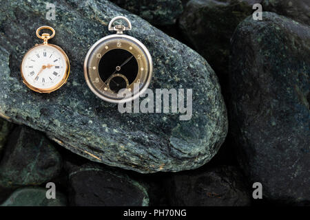 Einstellen der Uhren auf nassen grüne Steine mit einem Classic Gold Taschenuhr und eine schwarze und silberne Taschenuhr Stockfoto