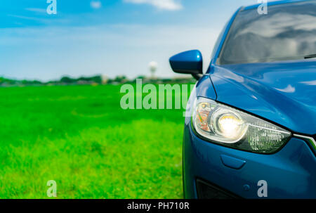Vorderansicht des Luxus blau Kompakt-SUV-Auto mit Sport und modernes Design auf grünem Gras Feld mit blauem Himmel und weißen Wolken geparkt. Hybrid auto und aut Stockfoto
