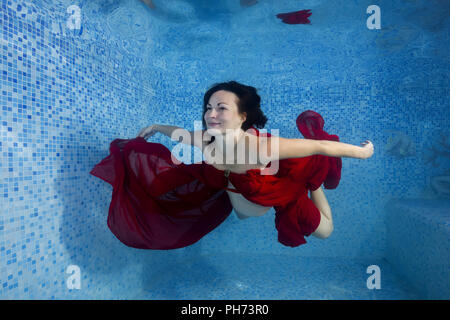 Schwangere Frau im roten Kleid unter Wasser im Pool posiert Stockfoto