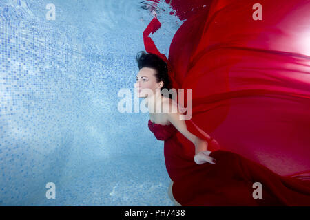 Schwangere Frau im roten Kleid unter Wasser im Pool posiert Stockfoto