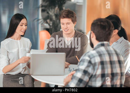 Positive junge Leute sitzen um den Tisch Stockfoto