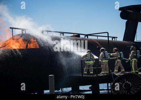 Feuerwehrmänner mit der 137 Special Operations Wing Feuerwehr- und Rettungsdienste, Oklahoma City, und die 138 Fighter Wing Feuerwehr, Tulsa, Oklahoma, kühle Metall Flugzeugstruktur, bevor ein Feuer während der Bereitstellung Readiness Training im März Air Reserve Base in Riverside County, Kalifornien, 28. Juni 2018 in Angriff zu nehmen. Der 137 Special Operations Tiefbau Squadron Mitglieder Zug auf regionaler Training Website alle drei Jahre als ein Teil dieser Deployment Readiness Training. Stockfoto