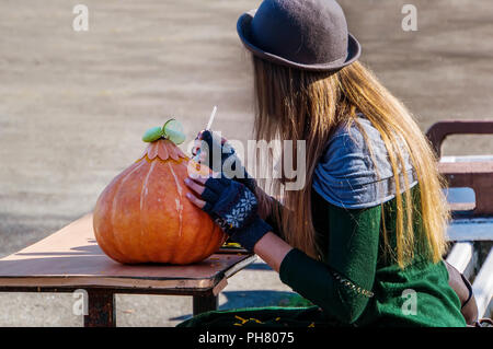 Junge Mädchen, Halloween Kürbis. Pre - Ferienbetreuung am Vorabend von Allerheiligen. Die Weibliche im Hut, der an einem Tisch auf der Straße schnitzt ihre pumpk Stockfoto