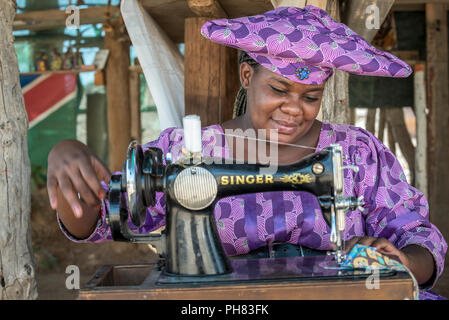 Native Herero Frau mit typischen Kopfbedeckungen und Kleidung ist an einer Nähmaschine sitzen, Kunene Region, Namibia Stockfoto