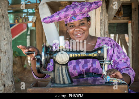 Native Herero Frau mit typischen Kopfbedeckungen und Kleidung ist an einer Nähmaschine sitzen, Kunene Region, Namibia Stockfoto