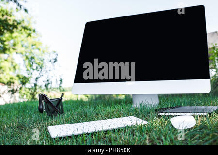 Selektiver Fokus von Lehrbuch und Computer mit leeren Bildschirm auf Gras im Freien Stockfoto