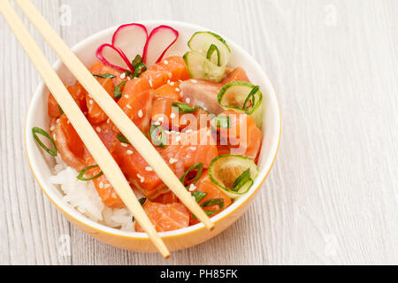 Hawaiian poke mit Lachs und Sesamsamen, gekochten Reis, frische Gurke, Radieschen und Frühlingszwiebeln in Porzellan Schüssel mit Holz- chopcticks. Ansicht von oben wi Stockfoto