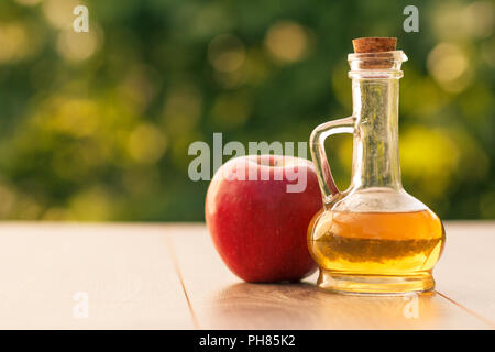Apfelessig in Glasflasche mit Korken und frischen roten Apfel auf Holzbrettern mit unscharfen grünen Hintergrund. Shellow Tiefenschärfe Stockfoto