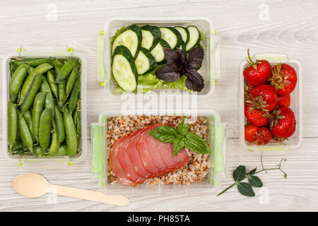 Kunststoff Mahlzeit prep Container mit Frische grüne Erbsen, Gurken und Salat, gekochten Buchweizen Brei und Scheiben von Fleisch, frische Erdbeeren und Holz- s Stockfoto