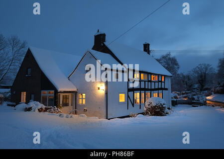 Starker Schneefall auf einem schwarz-weißen Häuschen in Longnor, Shropshire. Ein Twilght mit den Lichtern des Hauses glühen und reflektieren auf den Schnee draußen. Cottage im Besitz des Fotografen Stockfoto