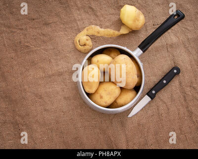 Zubereitung von Speisen, Schälen von Kartoffeln in rustikalem Ambiente Stilleben mit Topf, Messer, Hessische aka Jute. Ansicht von oben. Stockfoto