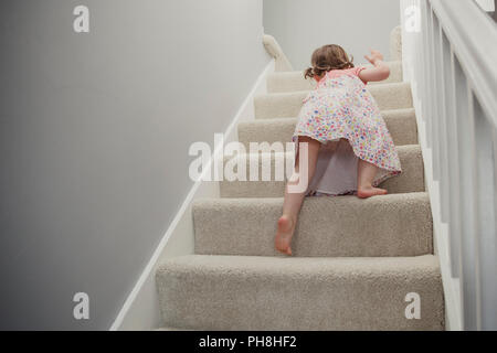 Ansicht von hinten von einem kleinen Mädchen klettern die Treppe im Haus. Sie ist die Erkundung und gehen auf ein Abenteuer rund um das Haus. Stockfoto