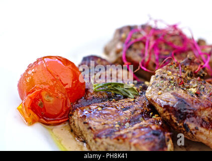 Drei Steaks mit gerösteten Tomaten und Stücke von rosa und grünen Salat auf einem weißen Teller Stockfoto