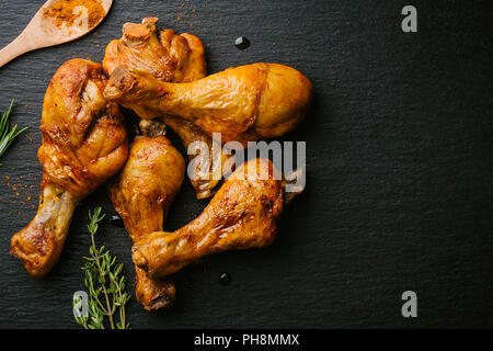 Lecker lecker geröstete bbq Hähnchenschenkel mit Gewürzen auf schwarzem Schiefer Hintergrund. Sicht von oben mit kopieren. Stockfoto