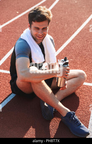 Lächelnd Sportler läuft im Stadion, ausruhen, halten Sie die Wärmflasche fertig Stockfoto
