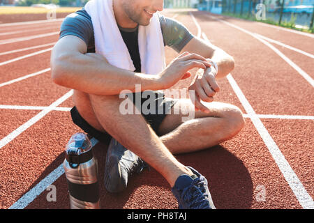 Lächelnd Sportler beendet im Stadion, Ausruhen, Wasserflasche, an smartwatch suchen Stockfoto
