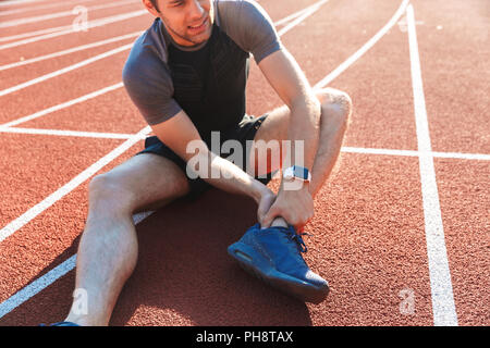 7/8 Bild einer müde Sportler von einem Knöchel Schmerzen im Stadion leiden Stockfoto