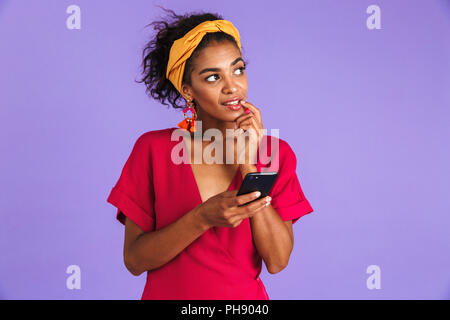 Geheimnis der afrikanischen Frau in Kleid holding Smartphone und entfernten Blick auf lila Hintergrund Stockfoto
