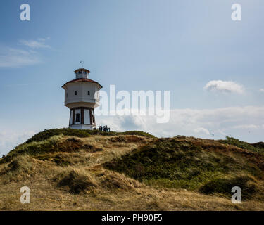 Wasserturm Langeoog. Deutschland, Deutschland. Ein Weg zu einer touristischen Attraktion führt, die ikonische White Water Tower - Wasserturm. Das Gras auf den Sanddünen haben von der Sonne gebleicht während der Hitzewelle dieses Sommers. Das Foto ist zurück - leuchtet ein Licht blauer Himmel und tiefe Schatten auf den Betrachter zu werfen Stockfoto