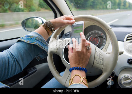 BOTTROP, Deutschland - 16.August 2018: Eine blonde Frau ist whatsapping auf Ihrem Smartphone, während Sie auf einer Autobahn in voller Geschwindigkeit fährt. Stockfoto